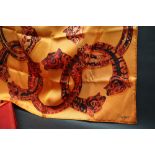 Cartier, a silk scarf, with interlocking leopards head bracelets to an orange ground, boxed,