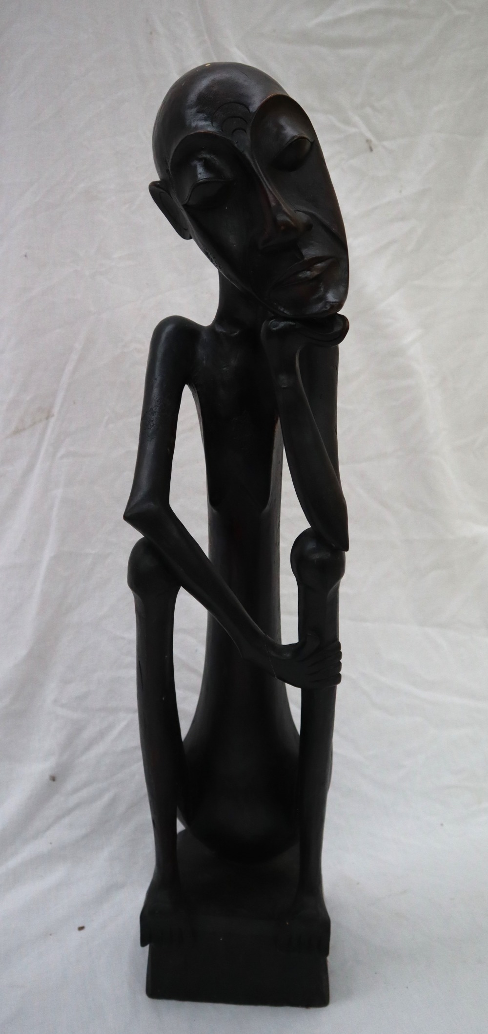 An African carving of a seated figure with his head resting on his right hand on a square plinth,