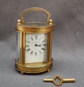 A brass carriage timepiece of oval form, with a scrolling handle the body decorated with scrolls,