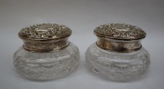 A pair of Elizabeth II silver topped and cut glass dressing table pots decorated with scrolls and