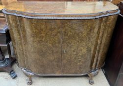 A burr walnut side cabinet with a shaped top and leaf border above two doors on carved cabriole leg