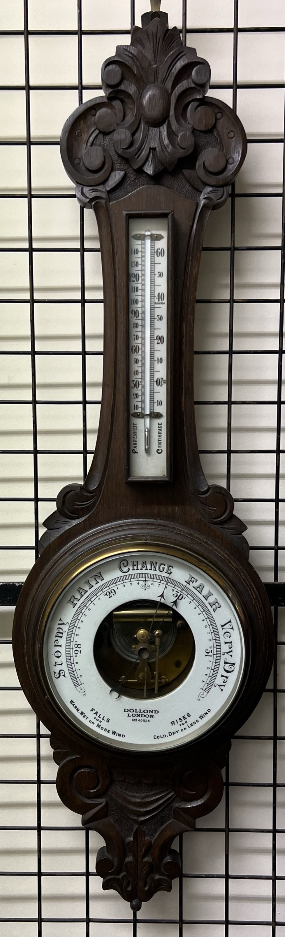 A carved oak aneroid barometer, with a mercury thermometer, pottery dial inscribed Dolland London,