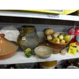 Four shelves of mixed items including a stoneware jug, tagines, a pair of vintage wooden bellows,