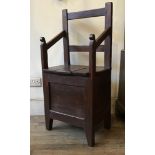 A 19th century varnished pine commode chair, with bar back, open arms and panelled front with