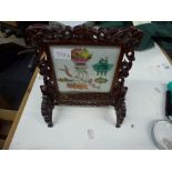 A Chinese carved hardwood table screen, inset with a famille rose porcelain plaque painted with '