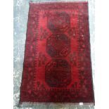A small wool rug made in Pakistan, the red ground with a line of three octagons [floor by saleroom