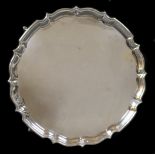 An Edwardian silver tray, of circular form with Chippendale pie crust edge, raised on four stepped