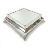 An early 20th century silver plated wedding cake stand, of square form with bevelled mirror surface,
