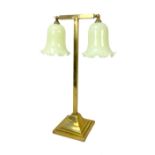 An Edwardian brass table lamp, with twin harebell-shaped lemon yellow opalescent shades issuing from