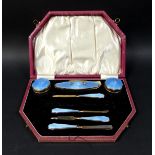 A cased silver dressing table set, serpentine edge lid with silver gilt and blue enamel