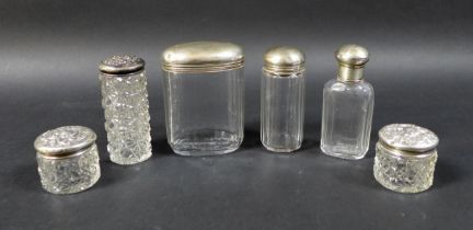 A collection of six silver-topped glass bottles, including two small jars with floral-patterned