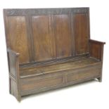 A 17th century oak box settle, with four panel back decoratively carved foliate and lunette