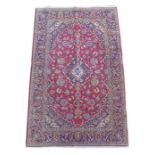 A Kashan rug, on red ground, with blue central lozenge, densely decorated ground with floral and