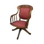An Edwardian oak office / desk swivel chair, with shaped arms, red leatherette seat and splat