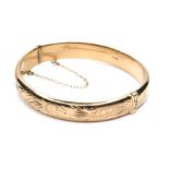 A 9ct gold hinged bangle,with floral bright cut engraved decoration, with safety chain attached,