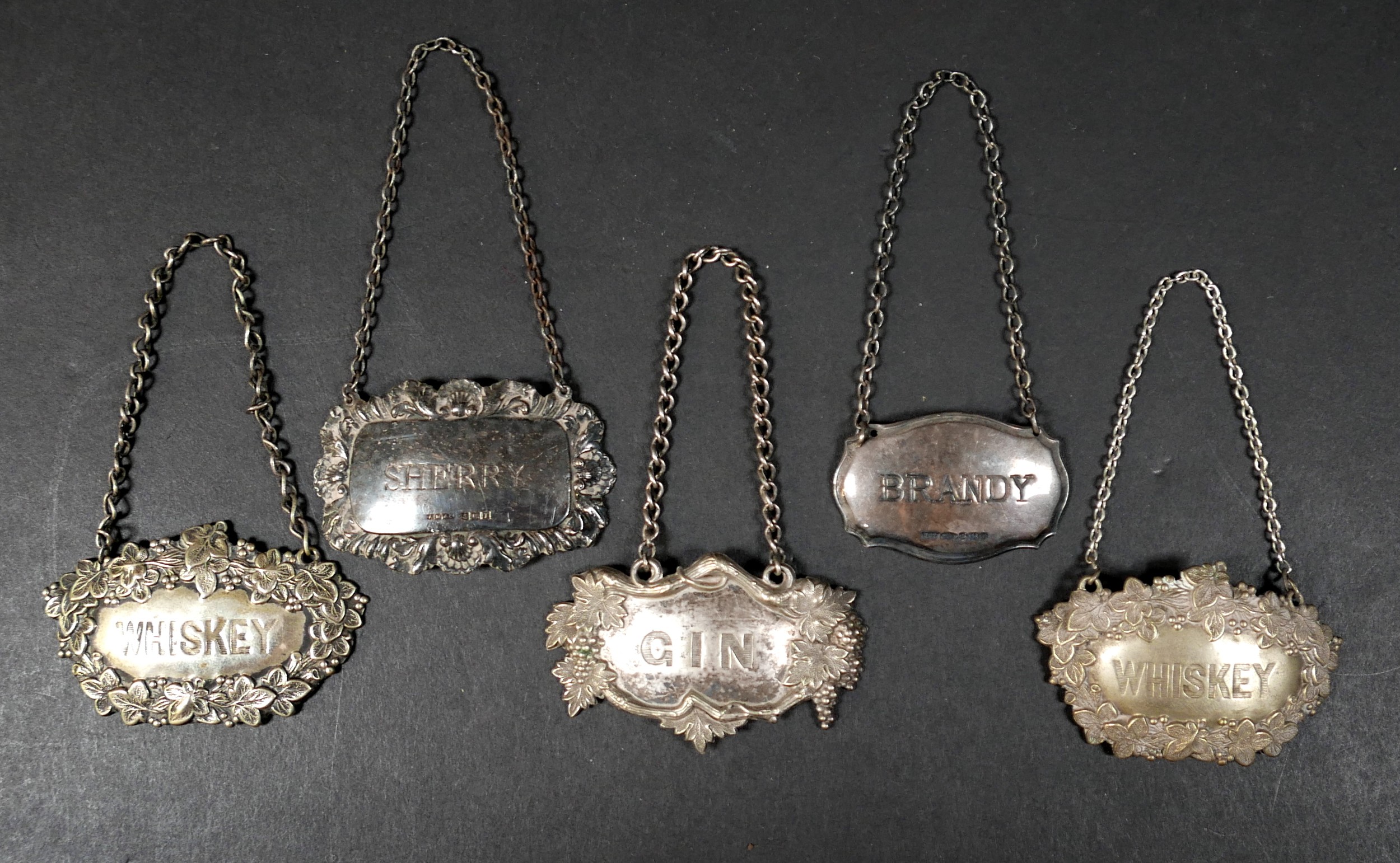 A group of five decanter labels, comprising a George V silver label of shield form with line