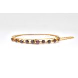 A GOLD AND GARNET OVAL HINGED BANGLE