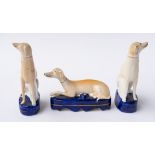 A STAFFORDSHIRE POTTERY RECUMBENT GREYHOUND PEN HOLDER AND A PAIR OF SEATED GREYHOUNDS (3)