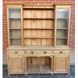 A tall antique pine kitchen dresser, the top with plate rack shelving flanked by glazed doors. The