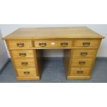An Edwardian light oak kneehole desk, housing an array of nine graduated drawers with brass drop