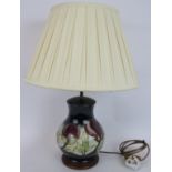 A Moorcroft Pottery lamp base in magnolia pattern with a cream pleated shade. Lamp height 36cm.