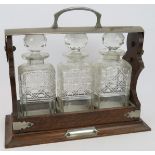 An Edwardian three decanter oak tantalus with silver plated mounts and lock (no key). Height 30cm.