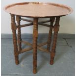 An Islamic brass topped Benares style table, featuring hand tooled designs, on folding ball turned