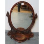 A Victorian mahogany oval swing vanity mirror, on carved and scrolled supports, the shaped plinth