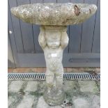 A nicely weathered reconstituted stone bird bath in the form of a shell held aloft by Putti.
