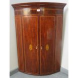 A George III mahogany bow fronted wall hanging corner cupboard with dentil cornice and marquetry