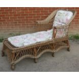 A vintage wicker chaise long, with shaped backrest and apron, raised on eight supports bound with