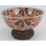 A finely decorated antique Japanese porcelain Imari bowl on carved wood stand, signed to base.