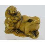 A Japanese carved ivory Netsuke, early 20th century featuring a frog and snake sitting on a lily