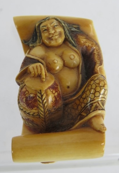 A finely carved Japanese ivory Netsuke, Meiji period, of a semi nude female on a scroll decorated in
