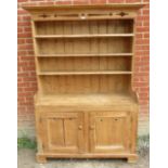 An antique pine kitchen dresser with carved and pierced cornice over plate rack shelving, over a