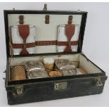 A 1920s picnic hamper in black leatherette case containing porcelain food boxes, wicker bound flasks