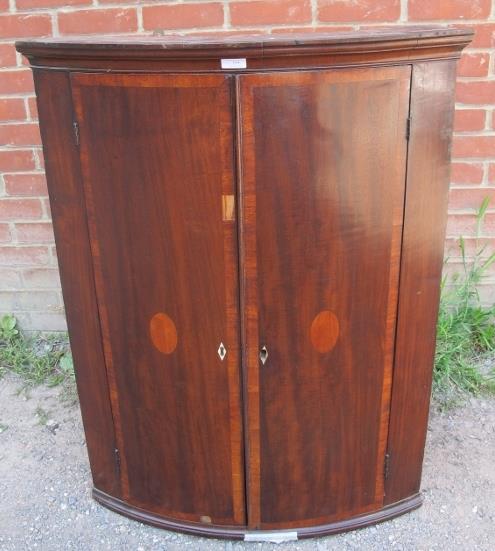 A George III mahogany bow fronted corner cupboard, with crossbanded inlay, housing four fitted