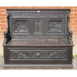 A 19th century oak box settle, ornate carved with relief panels depicting tavern scenes, acanthus