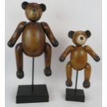 Two carved hardwood jointed teddy bears mounted on black wooden plinths. Tallest 62cm. (2).