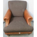 A large club armchair in the manner of Howard & son, upholstered in tan leather with brass studs and