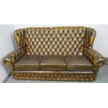 A vintage three-seater chesterfield wingback sofa, upholstered in buttoned green leather with