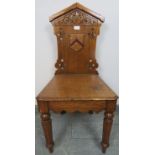A Victorian medium oak hall chair with carved and pierced backrest and applied shield decoration, on
