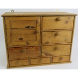 A small waxed pine cabinet of one cupboard and seven drawers with wooden knobs. Height 36cm. Width