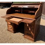 An early 20th century oak roll-top twin pedestal desk, the tambour door enclosing a fitted interior,