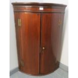 A George III mahogany bow fronted wall hanging corner cupboard, strung with satinwood, with 3 fitted