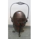 An Arts & Crafts copper coal/log bucket in a wrought iron cradle featuring scrolled and barley twist