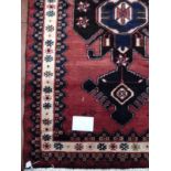 A Persian rug on red ground with central blue/black motif. 150cm x100cm (approx).