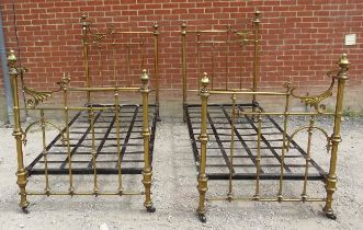 A pair of ornate antique brass single beds with asymmetric scrolled head and footboards featuring