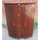 A George III mahogany bow fronted corner cupboard, with crossbanded inlay, housing four fitted