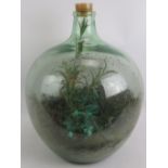 A large green glass carboy planted as a terrarium with a mix of real and artificial plants. Height